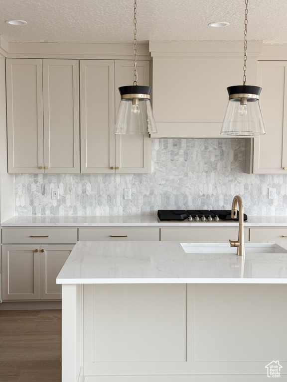 Kitchen featuring a textured ceiling, decorative backsplash, wood finished floors, light stone countertops, and hanging light fixtures