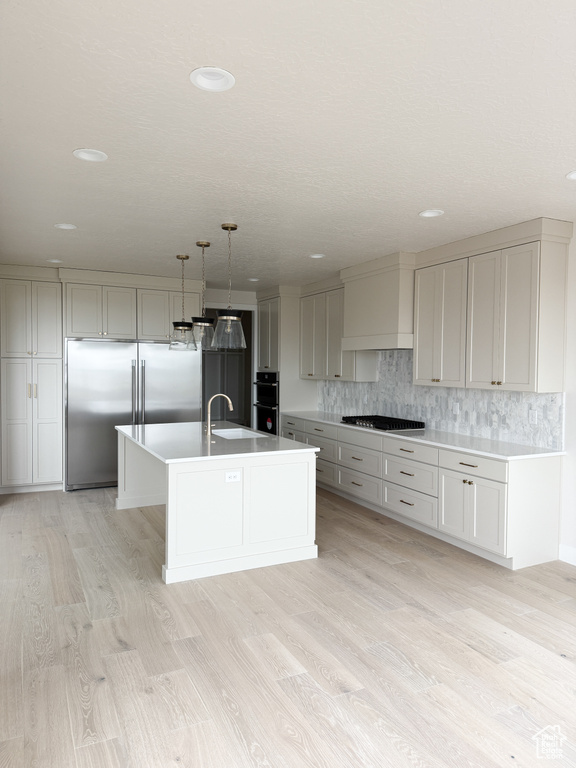 Kitchen featuring custom exhaust hood, a sink, decorative backsplash, stainless steel appliances, and light wood-style flooring