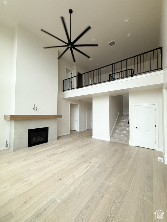 Unfurnished living room with a towering ceiling, visible vents, wood finished floors, stairway, and a tile fireplace