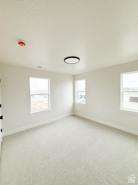 Unfurnished room featuring visible vents, baseboards, a textured ceiling, and light colored carpet