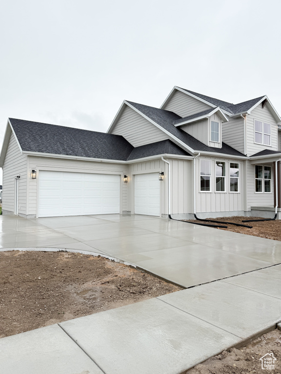 View of front facade featuring board and batten siding, an attached garage, driveway, and a shingled roof