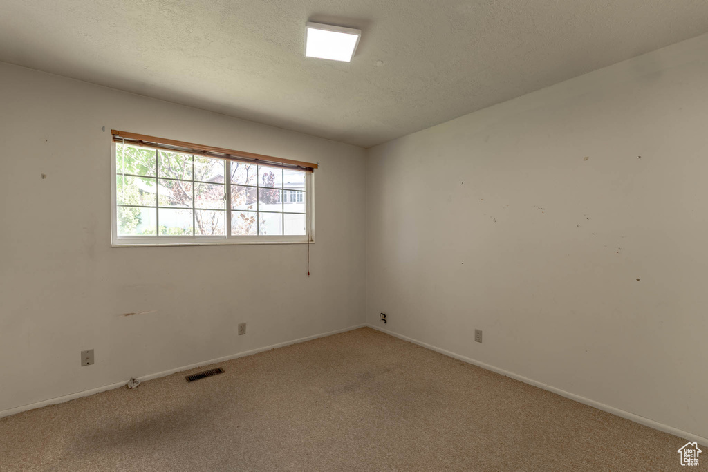 Spare room featuring a textured ceiling, baseboards, visible vents, and carpet