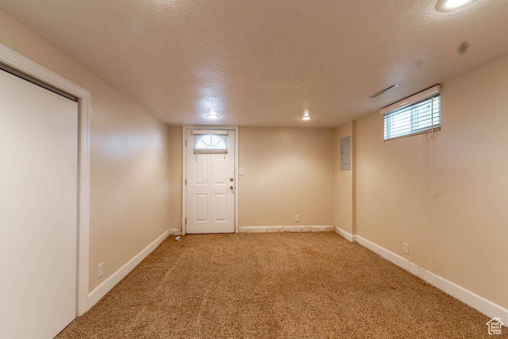 Basement featuring visible vents, light carpet, baseboards, a textured ceiling, and electric panel