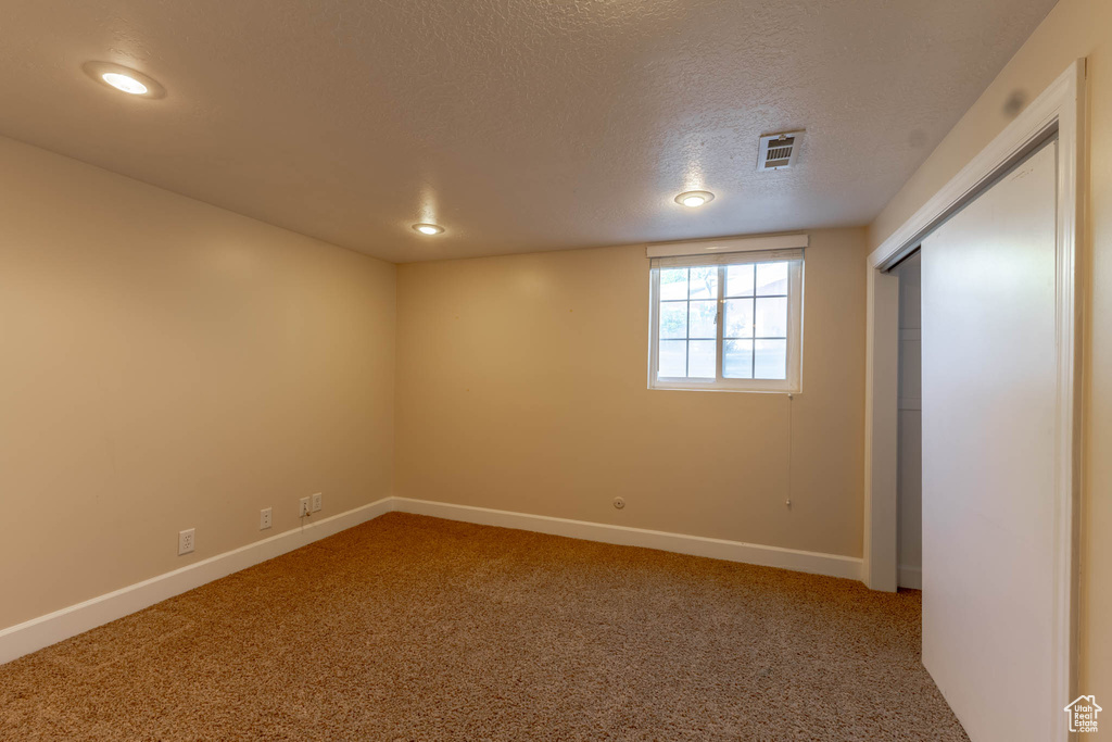 Below grade area featuring visible vents, baseboards, recessed lighting, a textured ceiling, and carpet