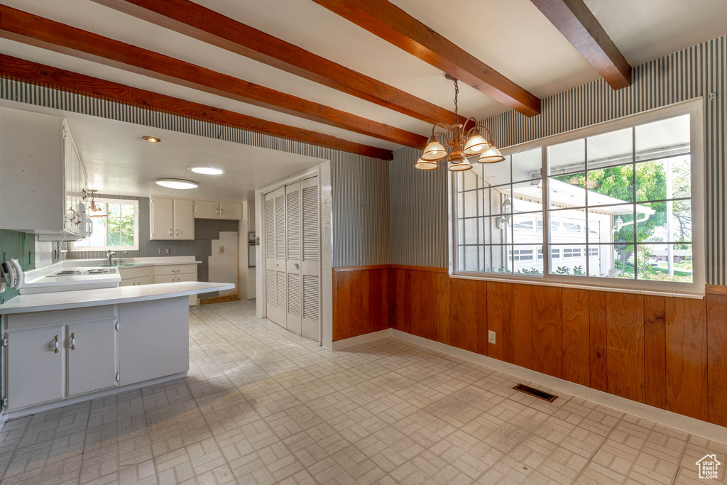 Kitchen featuring wainscoting, light countertops, wood walls, a chandelier, and brick patterned floor