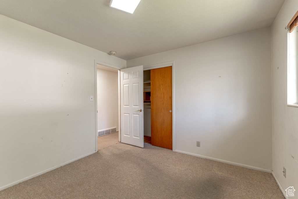 Unfurnished bedroom featuring light colored carpet, baseboards, visible vents, and a closet