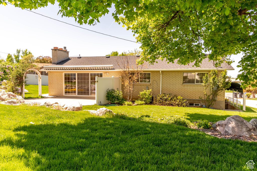 Rear view of house featuring brick siding, a patio area, fence, and a lawn