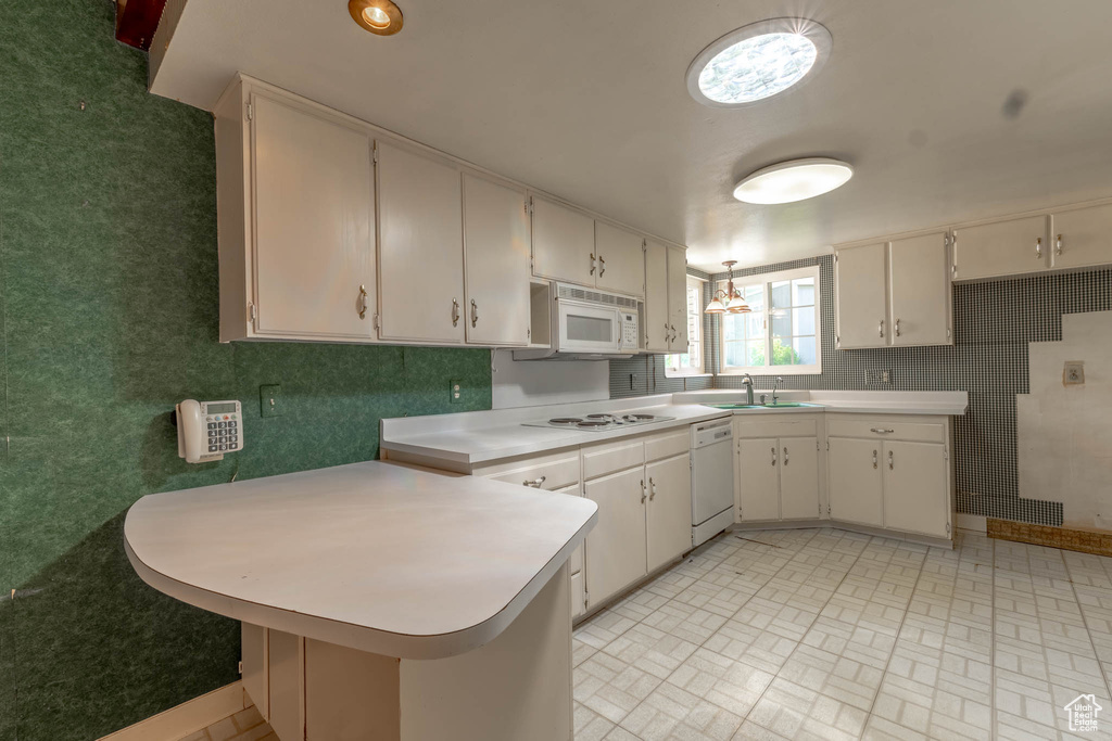 Kitchen featuring light countertops, a sink, white cabinets, a peninsula, and white appliances
