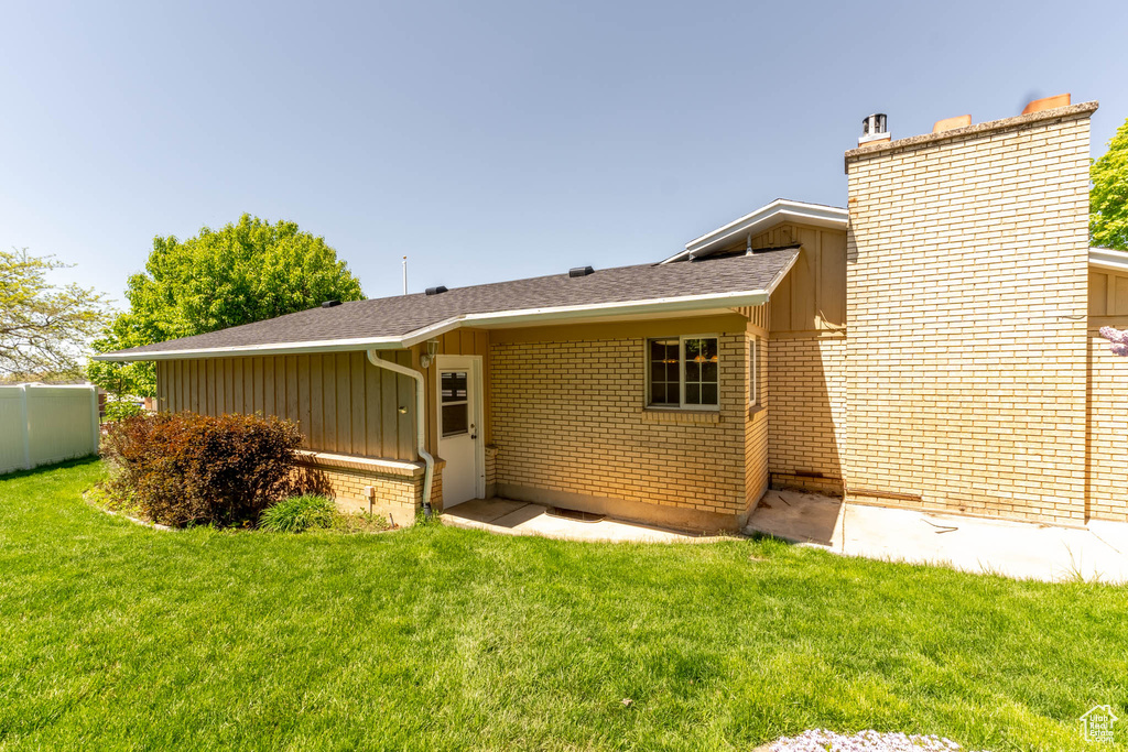Rear view of house featuring fence, a chimney, brick siding, board and batten siding, and a yard