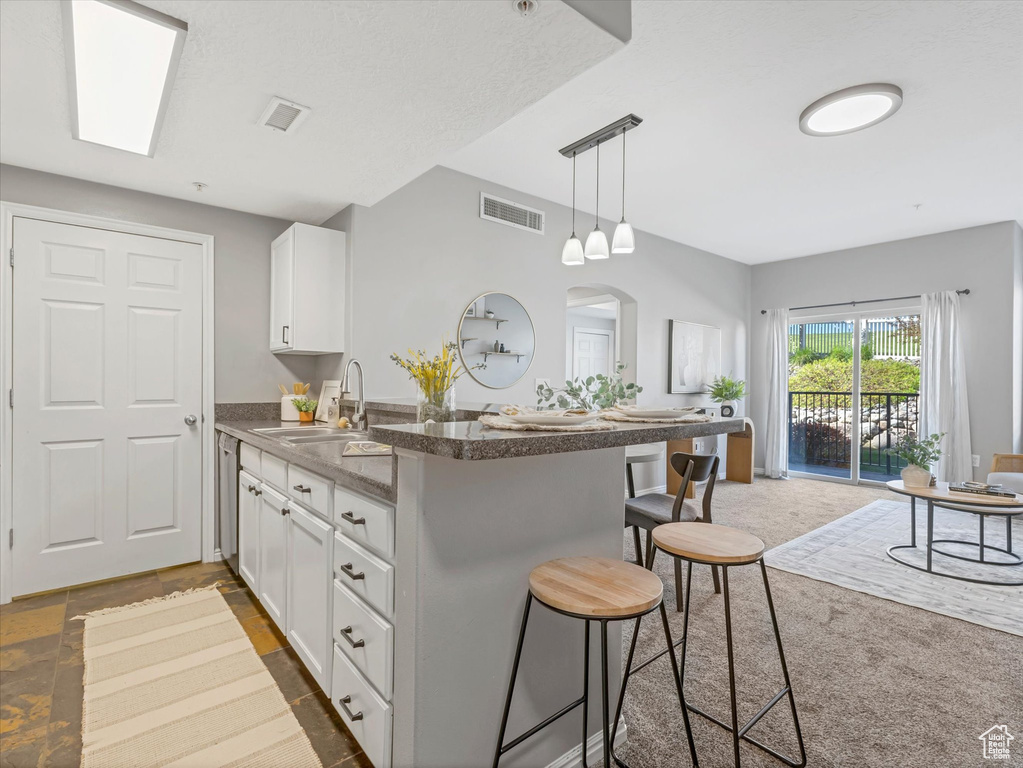 Kitchen featuring visible vents, a peninsula, a kitchen bar, white cabinets, and a sink