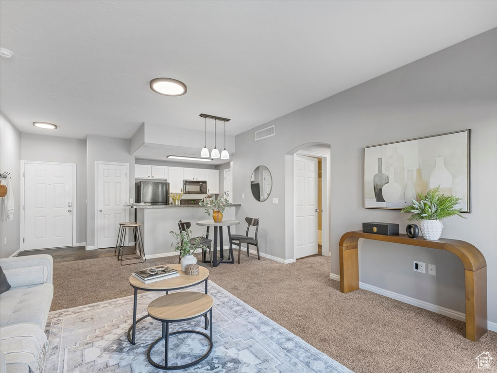 Living area featuring arched walkways, baseboards, visible vents, and light colored carpet