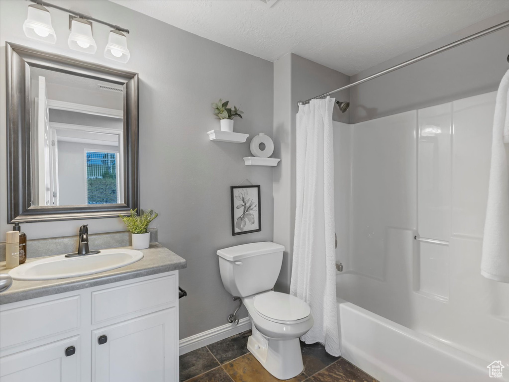 Bathroom featuring vanity, toilet, baseboards, a textured ceiling, and shower / tub combo