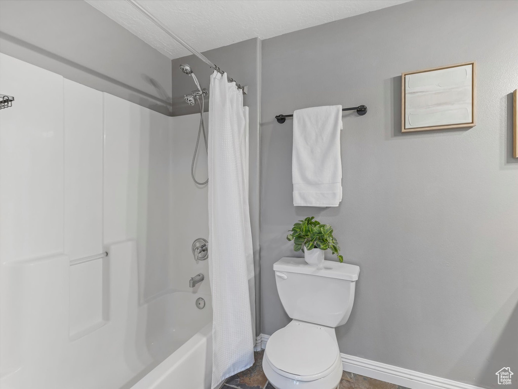 Full bathroom with toilet, a textured ceiling, shower / bath combination with curtain, and baseboards
