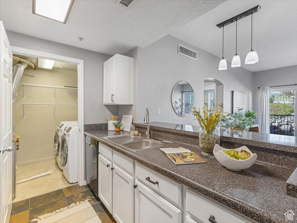 Kitchen with stainless steel dishwasher, white cabinets, washing machine and dryer, and a sink