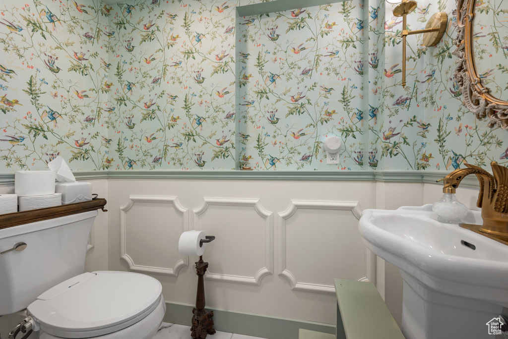 Half bath with a wainscoted wall, a decorative wall, wallpapered walls, and toilet