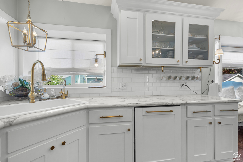 Kitchen featuring white cabinetry, decorative backsplash, a sink, and glass insert cabinets