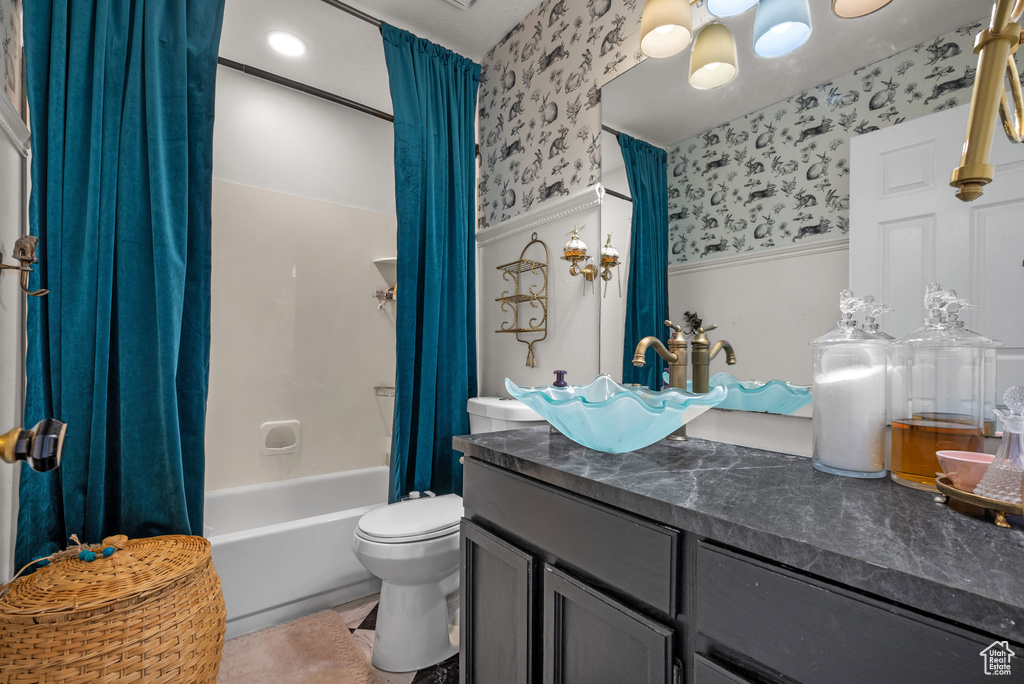 Bathroom with vanity, shower / bath combination with curtain, toilet, wallpapered walls, and a wainscoted wall