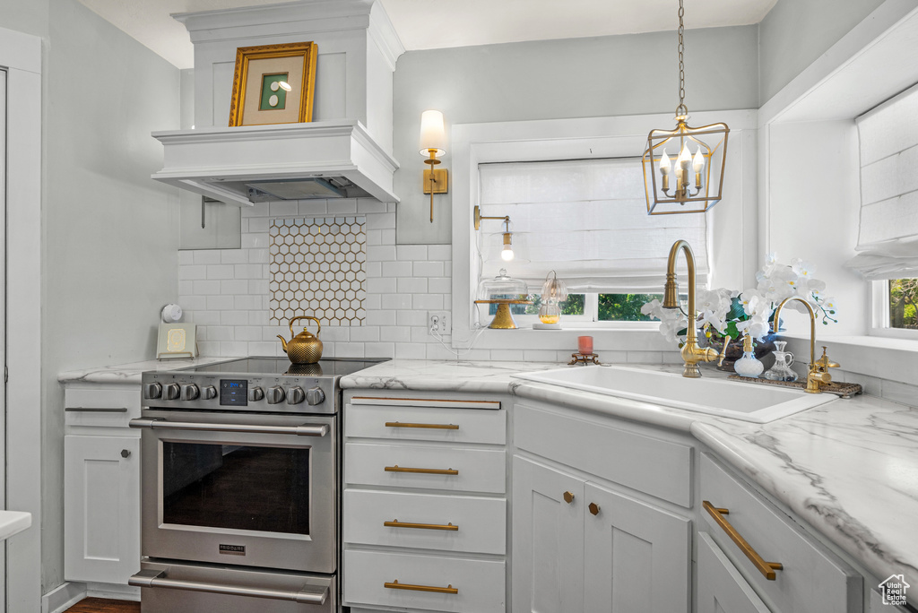 Kitchen with an inviting chandelier, a sink, custom range hood, backsplash, and stainless steel electric stove