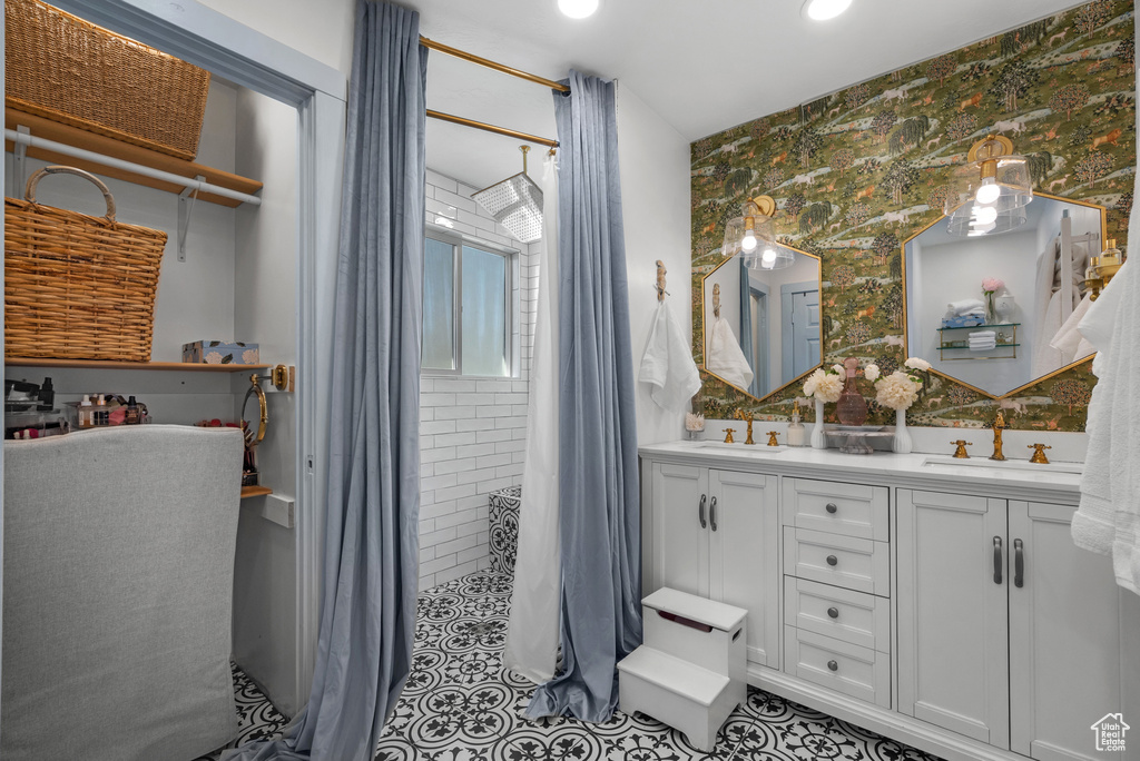 Bathroom with a sink, double vanity, wallpapered walls, and tiled shower