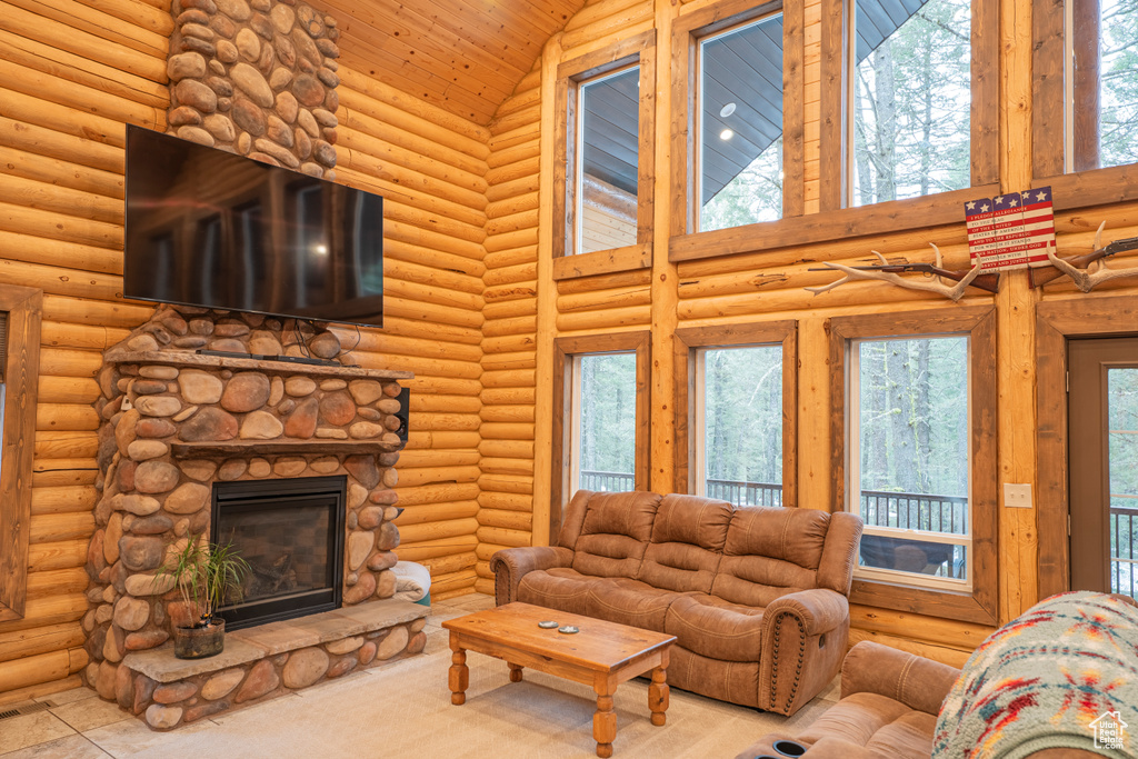 Living room with a healthy amount of sunlight, high vaulted ceiling, log walls, and a stone fireplace
