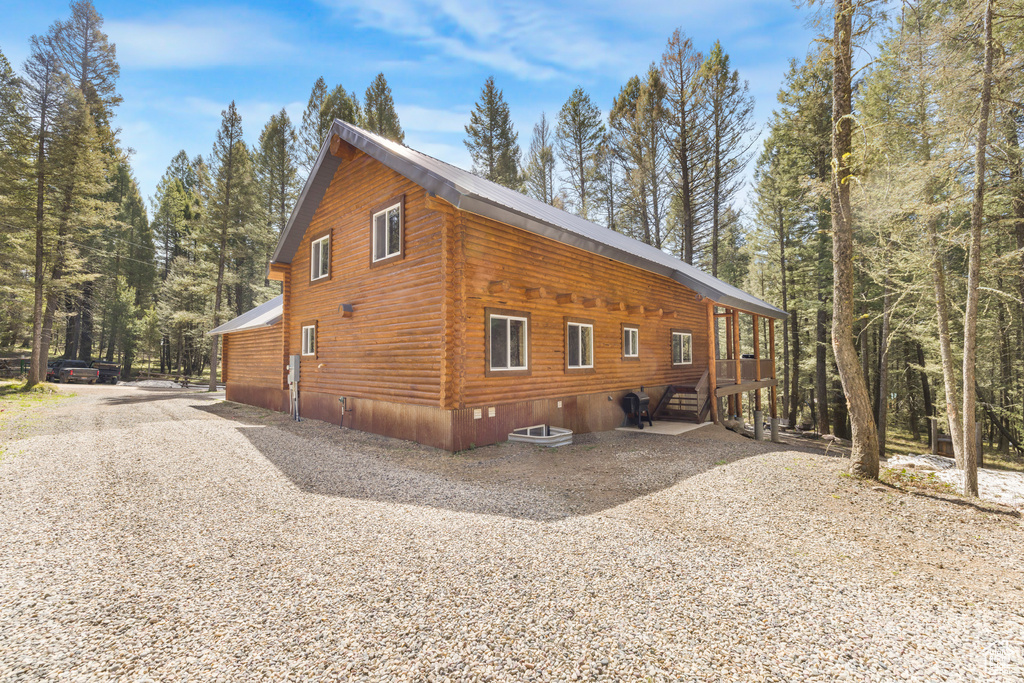 View of property exterior featuring log exterior, driveway, metal roof, and crawl space