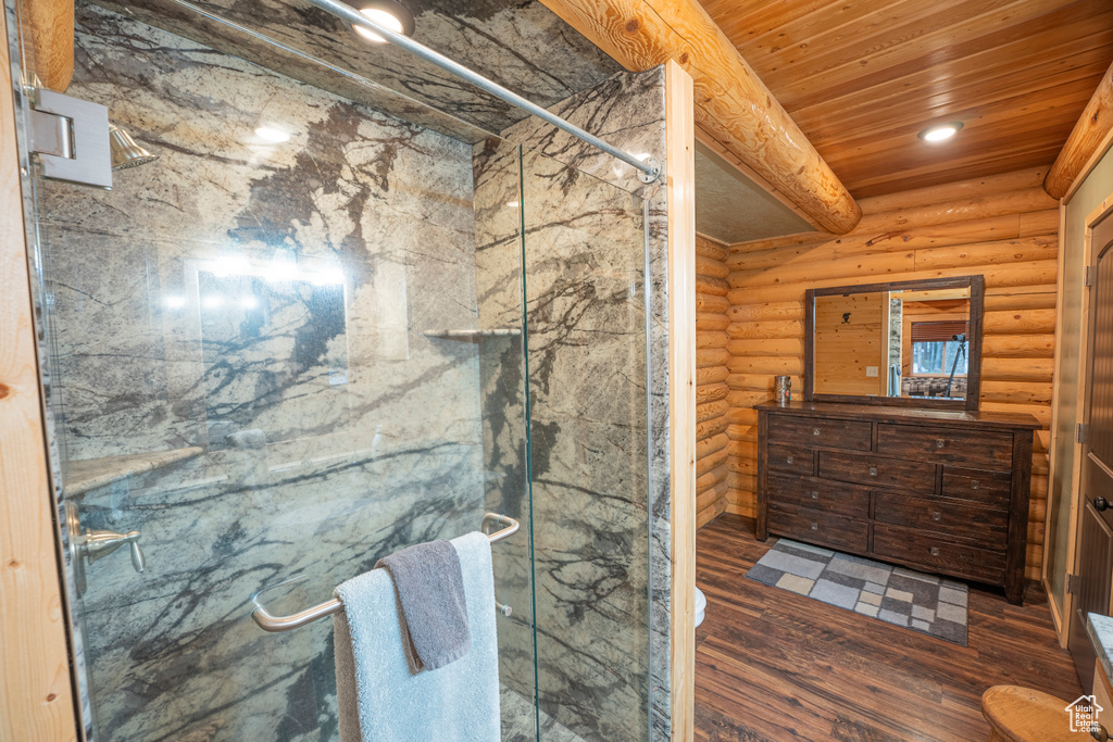 Full bath featuring wood finished floors, rustic walls, a marble finish shower, and vanity