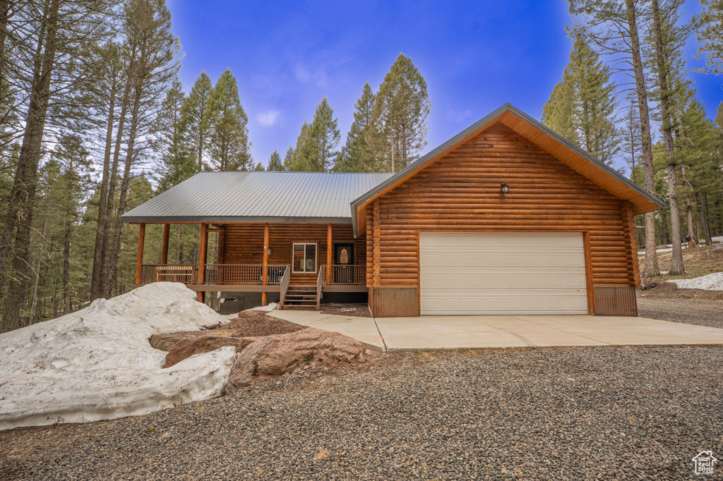 View of front of home with log siding, a garage, gravel driveway, covered porch, and metal roof