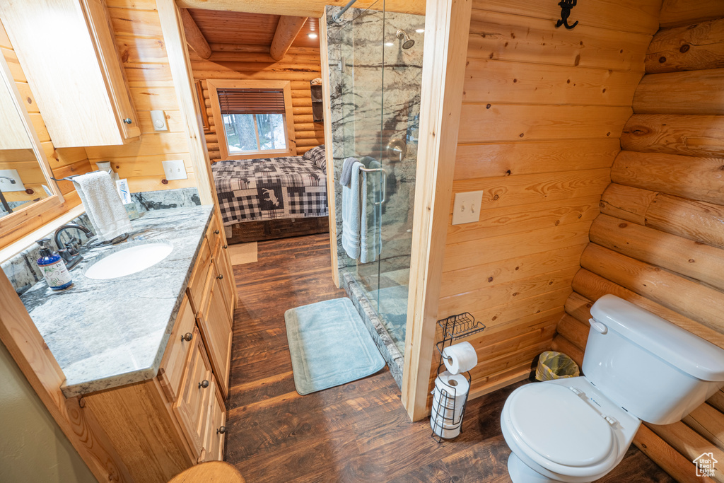 Bathroom with log walls, a stall shower, toilet, and wood finished floors
