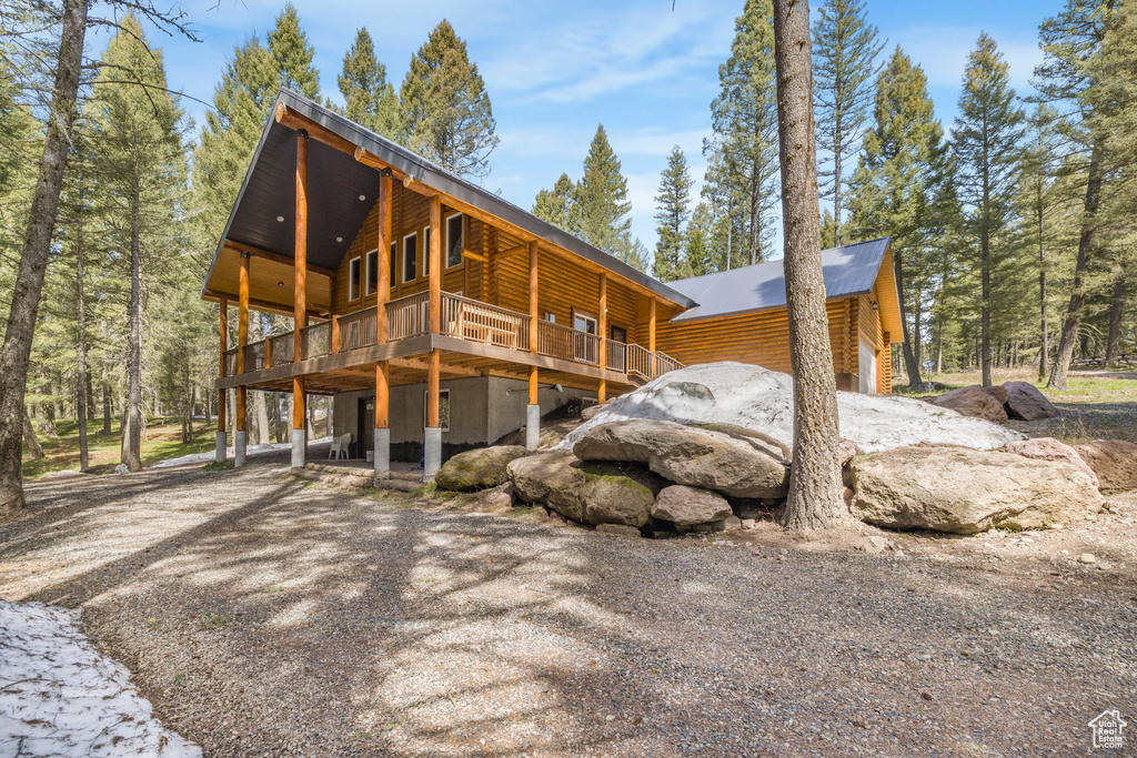 View of side of home featuring driveway, a wooden deck, log veneer siding, and a carport