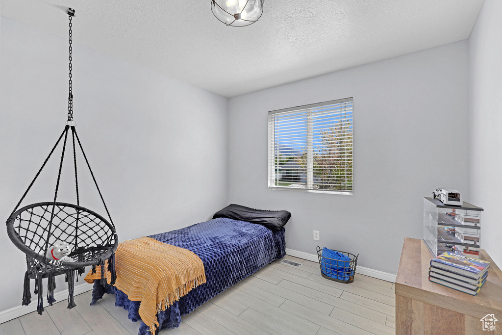 Bedroom featuring baseboards, light wood-style flooring, a textured ceiling, and visible vents