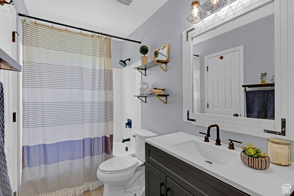 Bathroom featuring vanity, shower / bathtub combination with curtain, and toilet