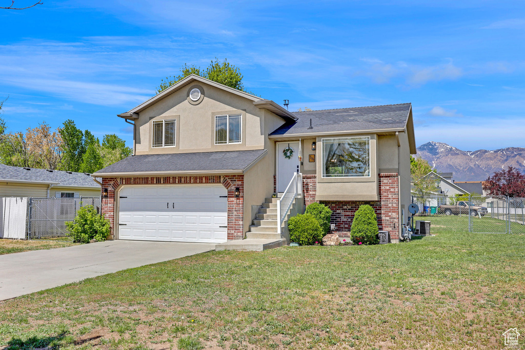 Tri-level home featuring an attached garage, fence, driveway, and stucco siding