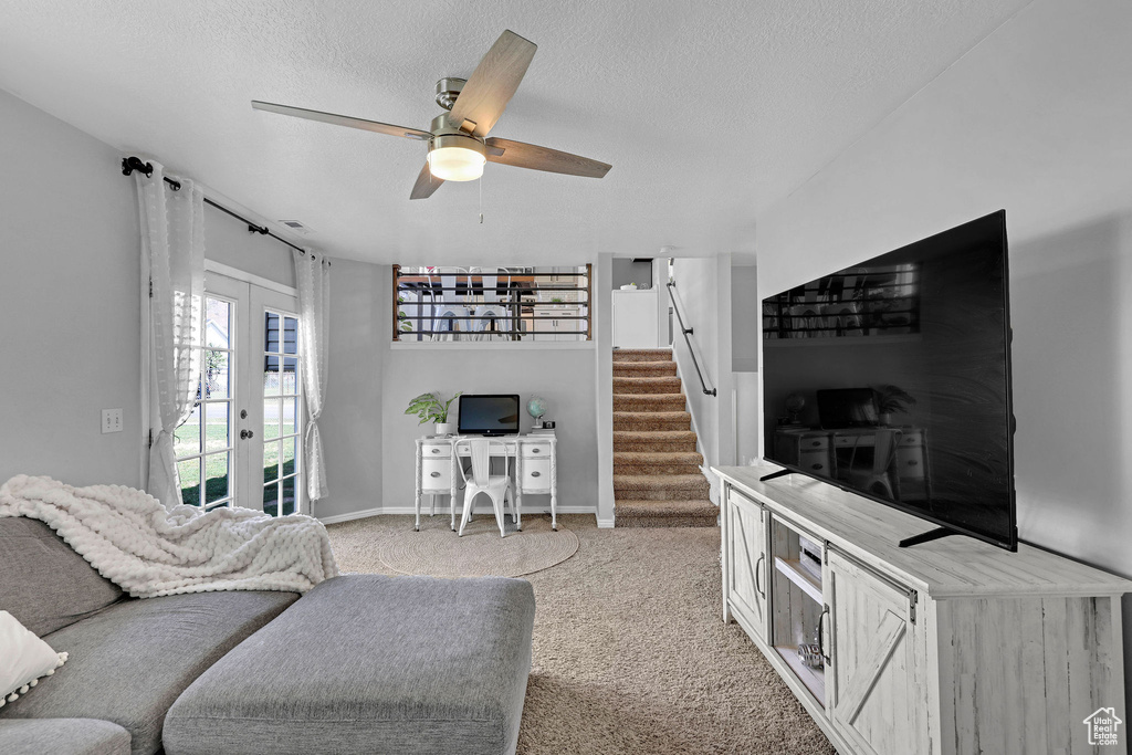 Carpeted living area featuring stairs, baseboards, ceiling fan, a textured ceiling, and french doors