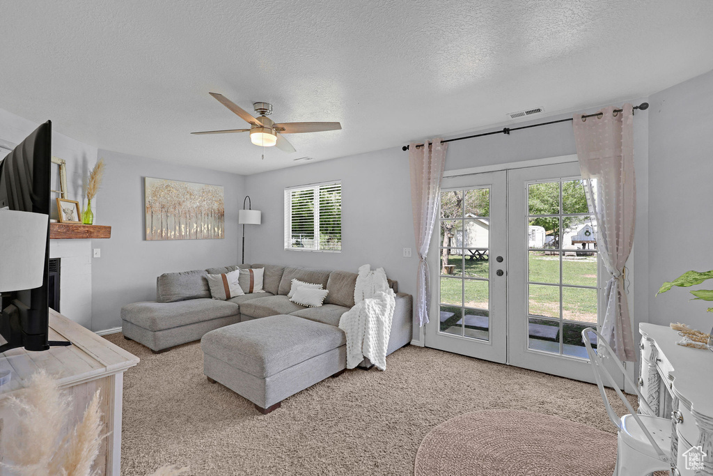 Living room with visible vents, a textured ceiling, french doors, a ceiling fan, and carpet