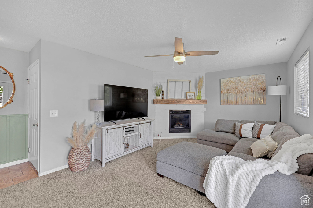 Living area with a ceiling fan, light colored carpet, visible vents, a large fireplace, and baseboards