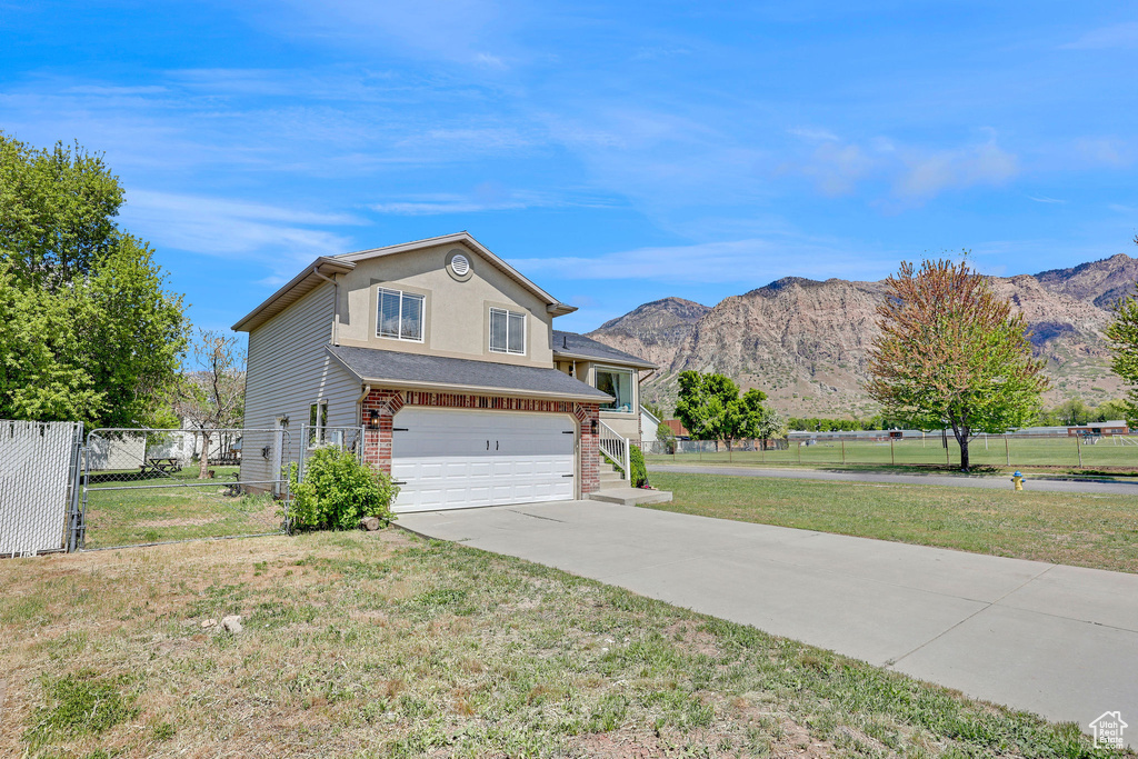 View of front of property featuring an attached garage, driveway, a mountain view, and a front lawn