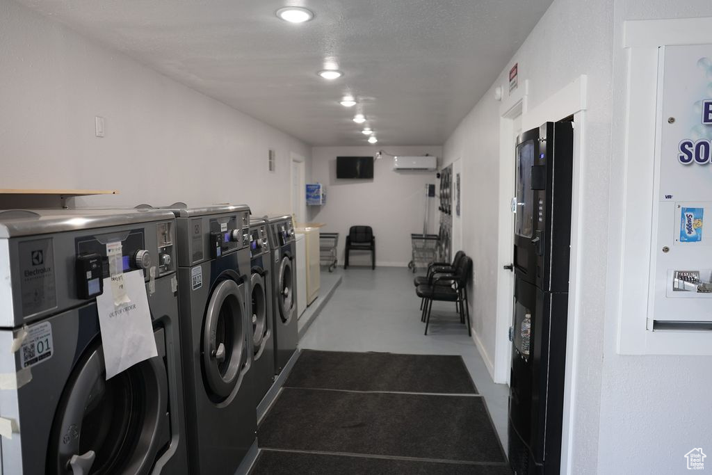 Shared laundry area with stacked washer / dryer, an AC wall unit, baseboards, and washer and clothes dryer