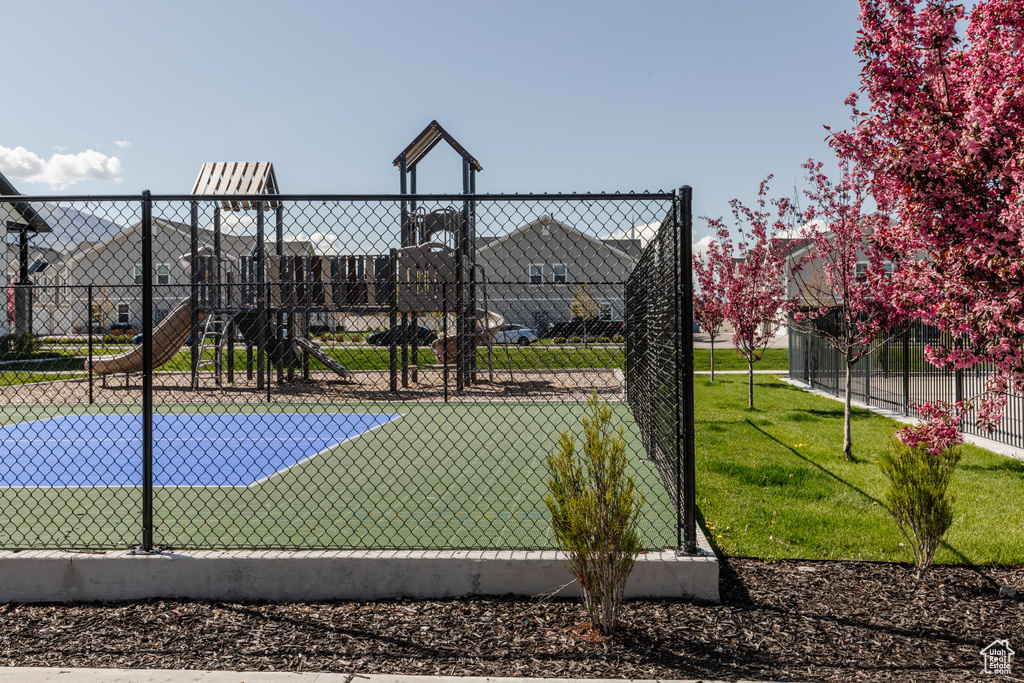 View of sport court featuring fence and a lawn