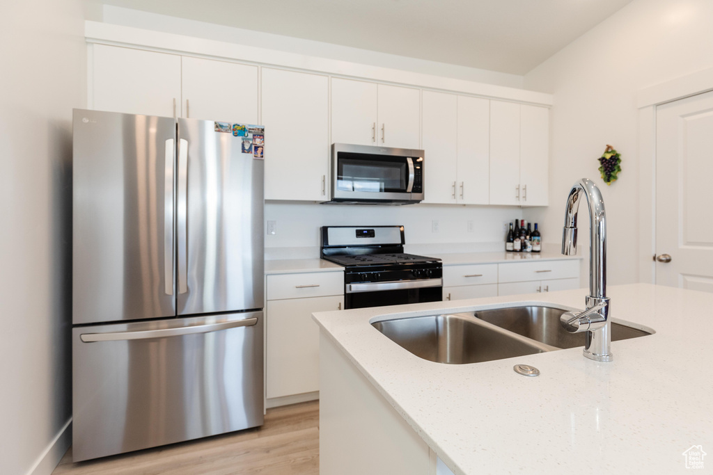 Kitchen featuring white cabinets, light stone countertops, appliances with stainless steel finishes, a sink, and light wood-type flooring