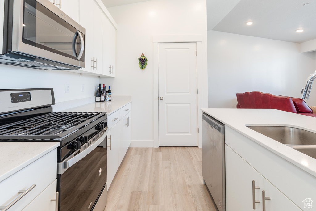 Kitchen with a sink, light wood-style floors, stainless steel appliances, recessed lighting, and white cabinetry