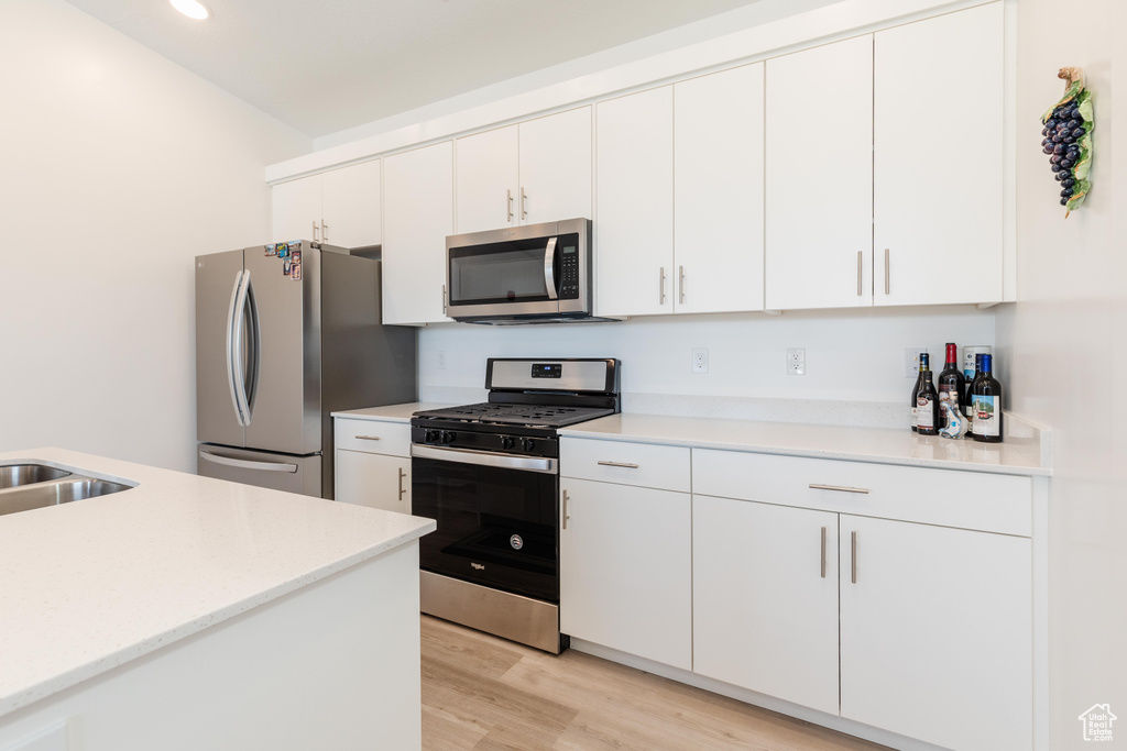 Kitchen with appliances with stainless steel finishes, a sink, white cabinets, light wood finished floors, and recessed lighting