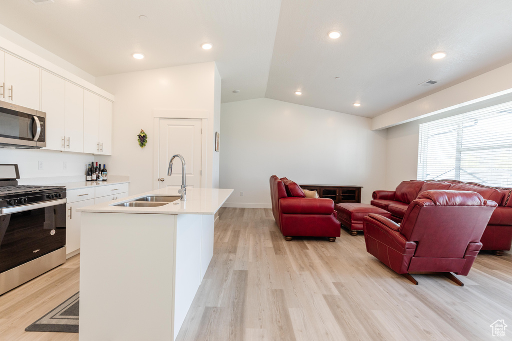 Kitchen featuring a sink, light wood finished floors, appliances with stainless steel finishes, and lofted ceiling