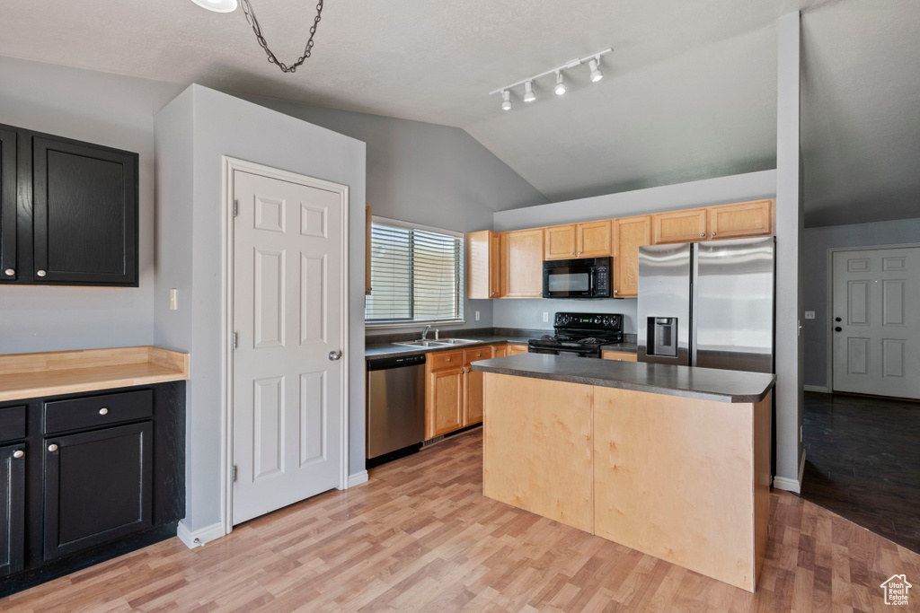 Kitchen with a sink, light wood finished floors, dark cabinetry, vaulted ceiling, and black appliances
