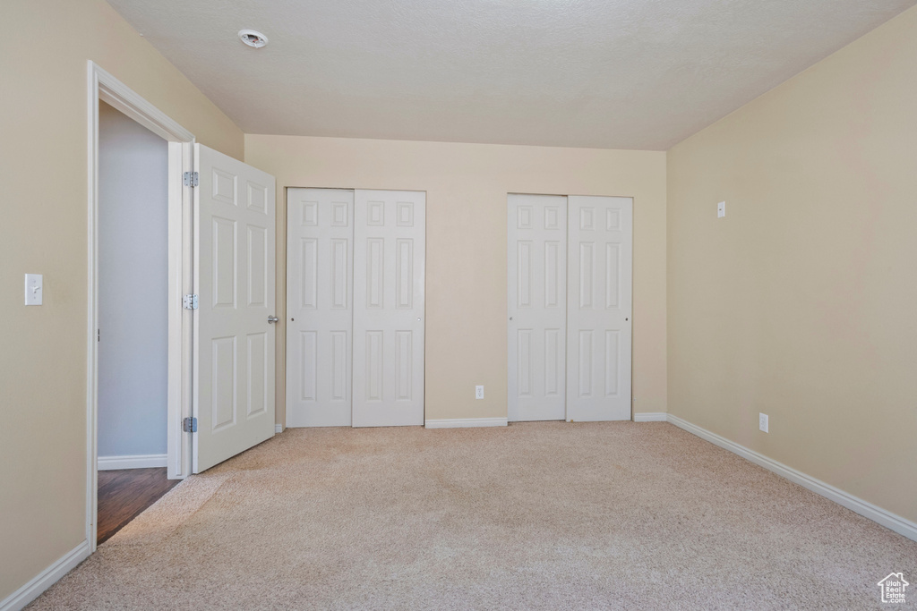 Unfurnished bedroom with two closets, carpet flooring, and baseboards