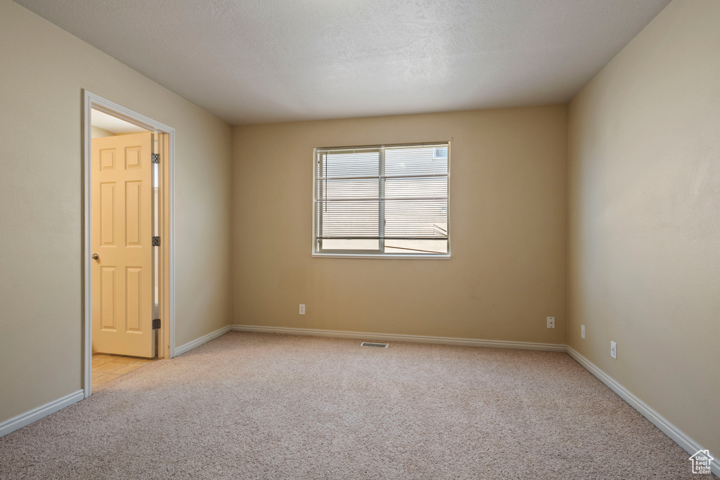 Spare room with baseboards, visible vents, and light colored carpet