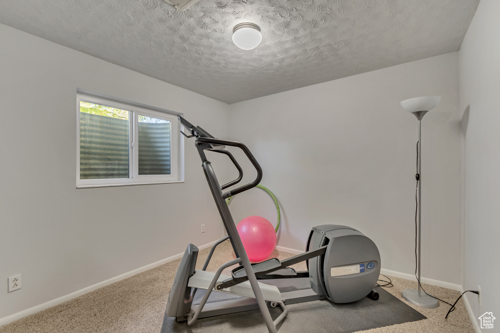 Exercise area featuring baseboards, a textured ceiling, and carpet
