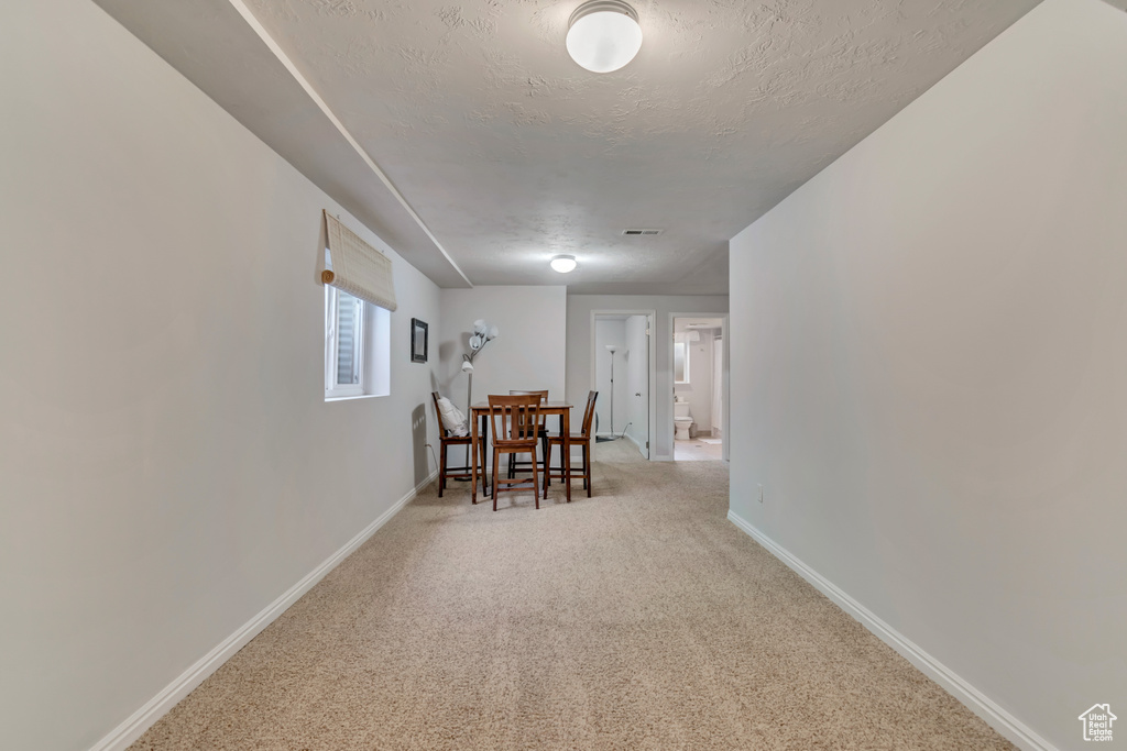 Corridor featuring baseboards, a textured ceiling, visible vents, and light carpet