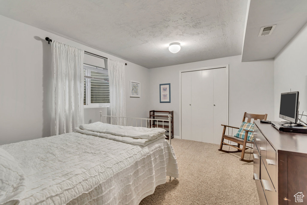 Carpeted bedroom with a closet, a textured ceiling, and visible vents