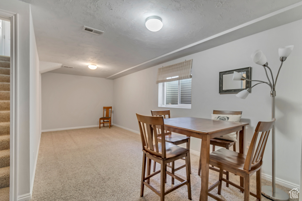 Dining area featuring carpet flooring, a textured ceiling, visible vents, and stairway
