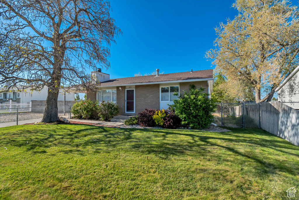 Back of house with brick siding, a lawn, fence, and a chimney